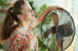 Une femme face à un ventilateur pour se refroidir
