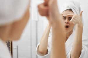 Une femme découvrant un bouton d'acné devant son miroir